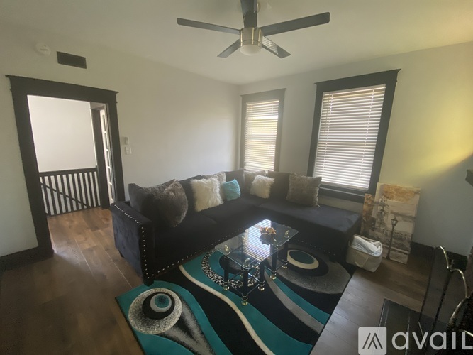 A living room with a black couch and a rug with a spiral design on it.