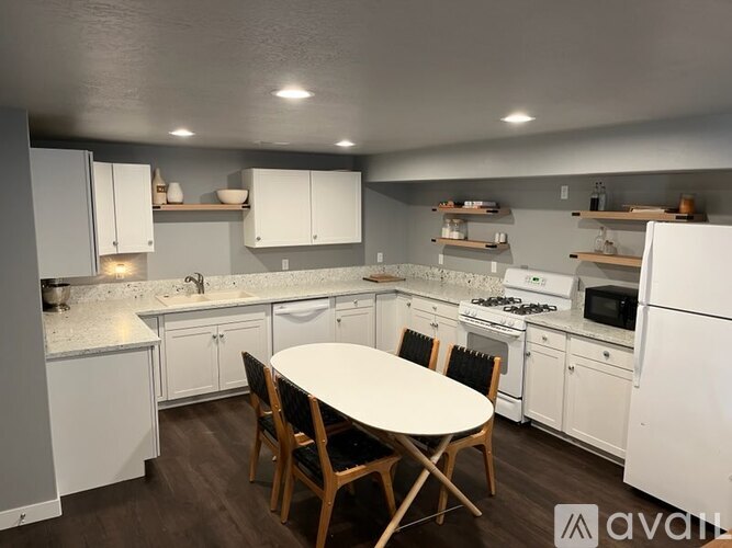 A kitchen with white appliances and wooden chairs.