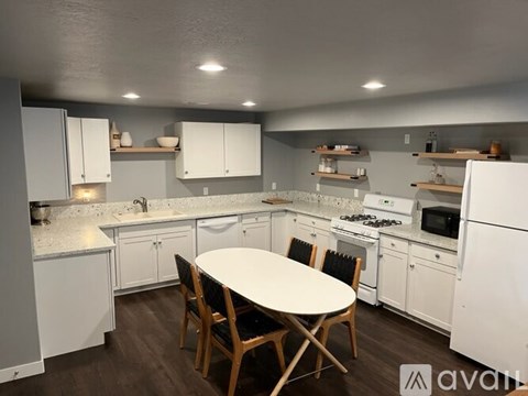 A kitchen with white appliances and wooden chairs.