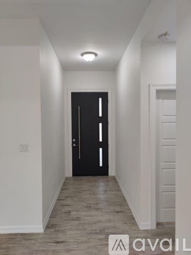 A hallway with a black door and wooden flooring.