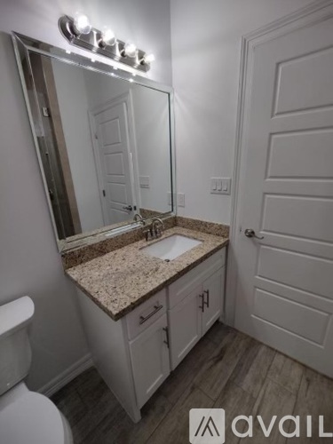 A bathroom with a granite countertop and a mirror with lights above it.