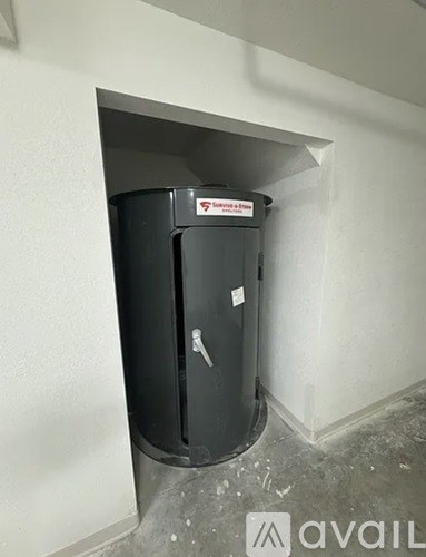 A black trash can with a red label on it is in a white wall.