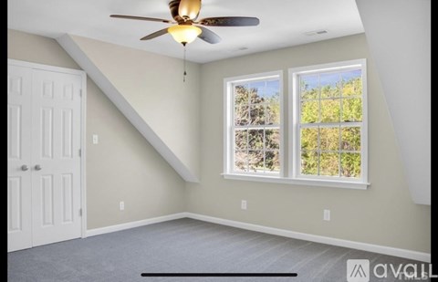 A room with a ceiling fan and two windows.