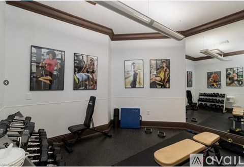 A gym room with a variety of equipment including dumbbells, weight plates, and a bench.