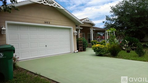 A house with a white garage door and a green trash bin in front of it.