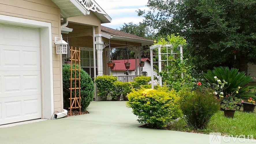 A white garage door is on the left of a house with a white pergola.