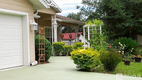 A white garage door is on the left of a house with a white pergola.