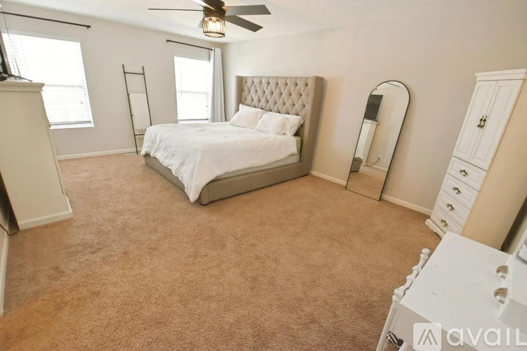 A bedroom with a large bed, a ceiling fan, and a window with blinds.
