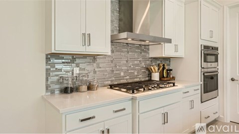 A kitchen with white cabinets and a stone backsplash.