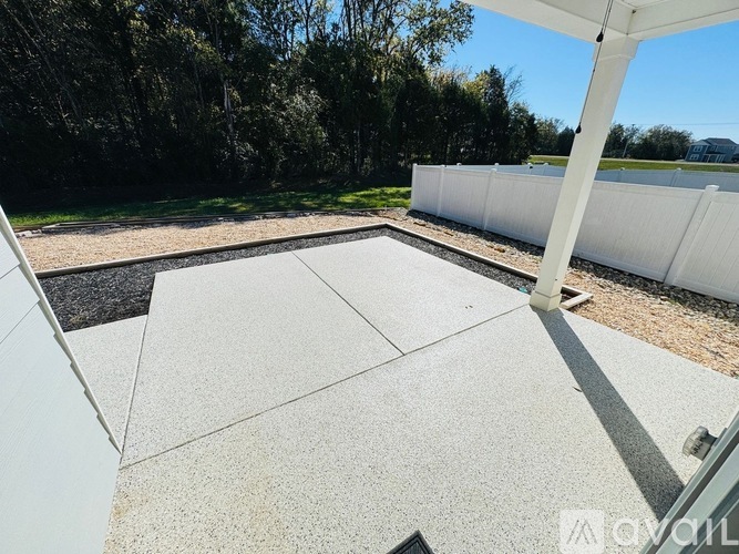 A patio with a white fence and trees in the background.