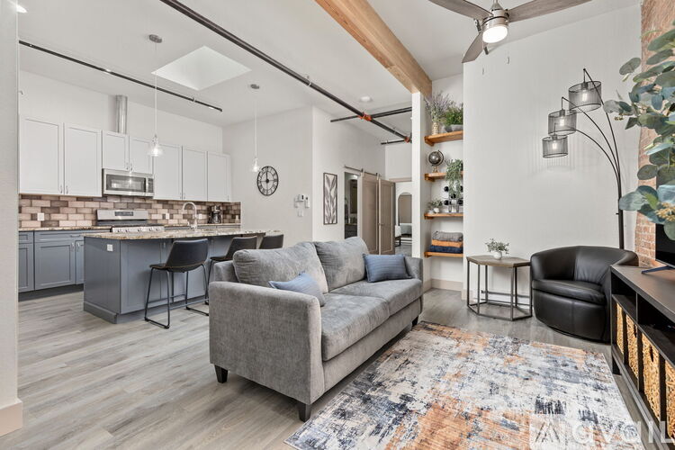 A modern living room with a grey sofa and a kitchen area in the background.
