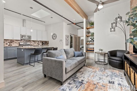 A modern living room with a grey sofa and a kitchen area in the background.