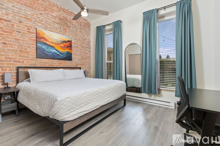 A bedroom with a bed, desk, and a painting on the wall.