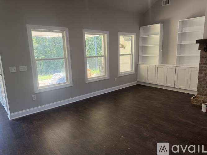 A room with three windows and a fireplace with shelves on the wall.