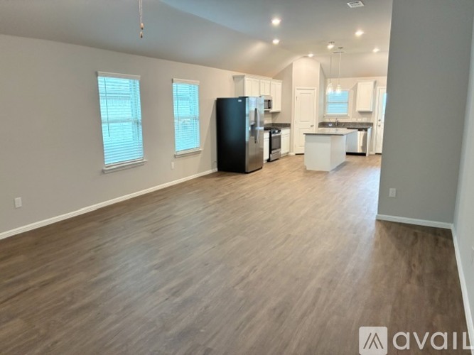 A spacious room with wooden flooring and a kitchen area in the background.