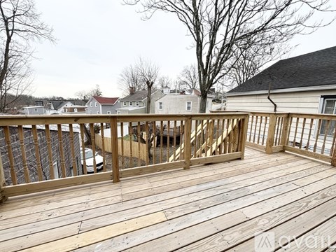 A wooden deck with a railing and a car parked in the background.