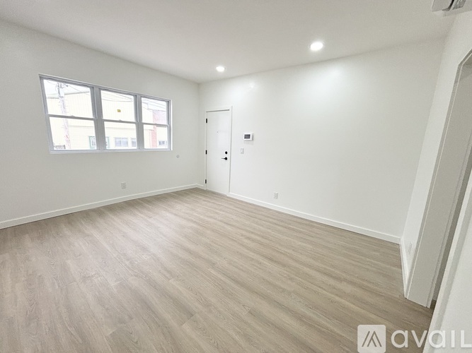 A spacious room with light wood flooring and a white door.