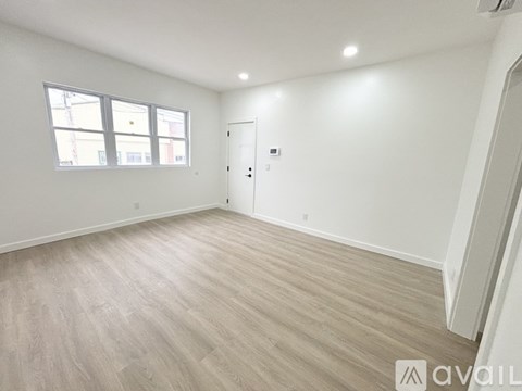 A spacious room with light wood flooring and a white door.