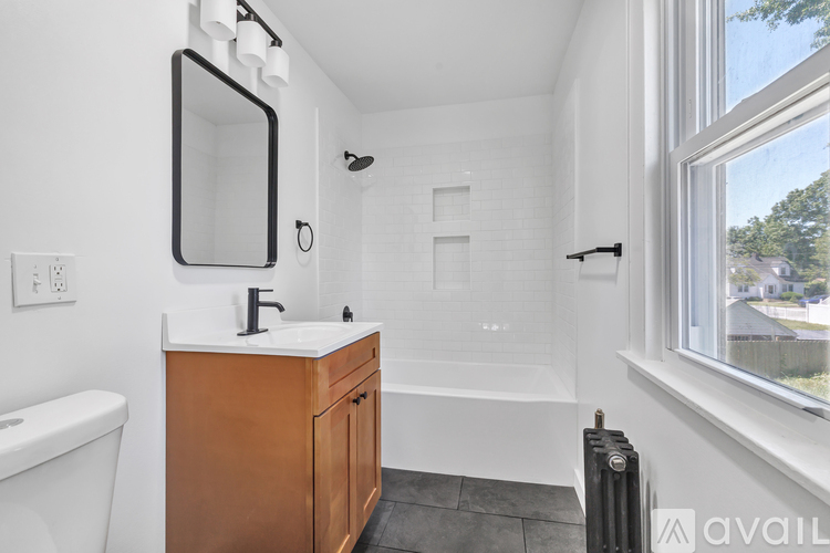 A bathroom with a white tub, a wooden vanity, and a window.