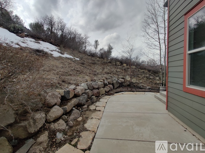A stone wall borders a concrete walkway leading to a house.