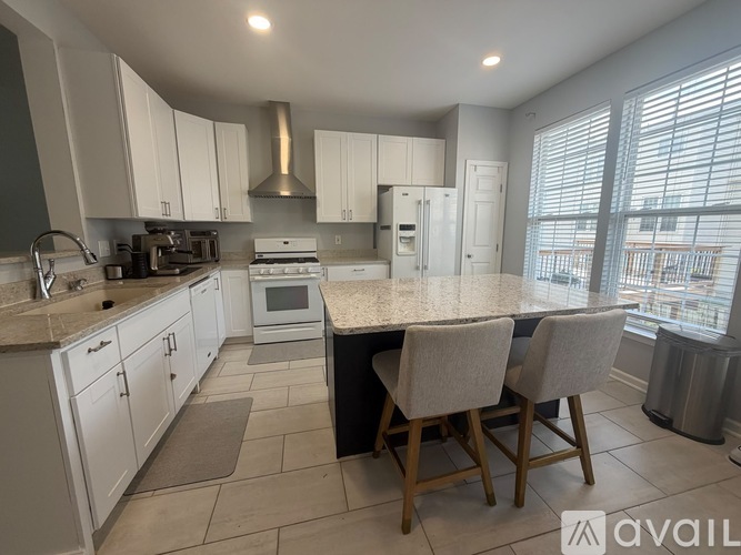 A kitchen with white cabinets and a large island with two chairs.