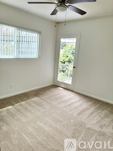 A room with a carpeted floor, a ceiling fan, and a door leading to a balcony.