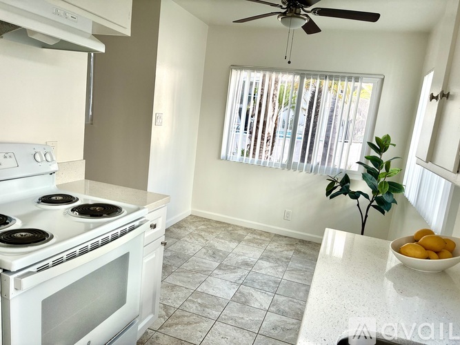 A white stove top oven with four burners and a fan is in a kitchen with a bowl of fruit on the counter.