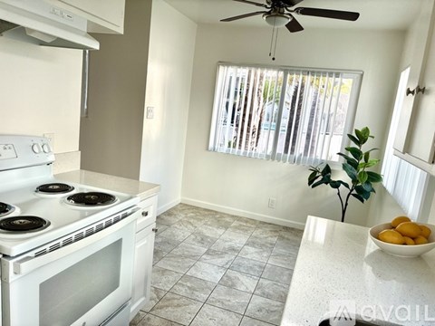 A white stove top oven with four burners and a fan is in a kitchen with a bowl of fruit on the counter.