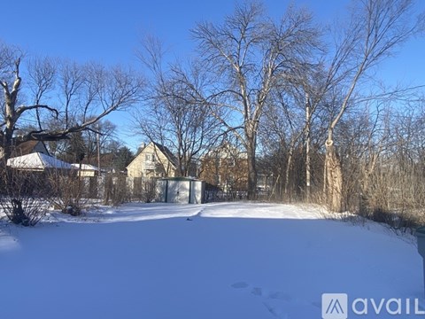 A snow-covered field with trees and a house in the background.