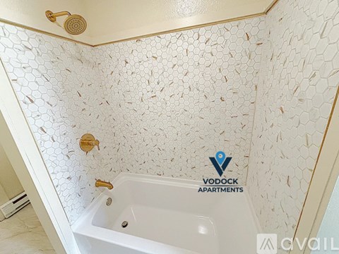 A Vodock Apartments shower with a white tub and gold fixtures.