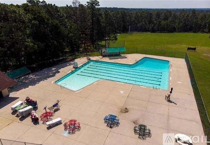 A large outdoor swimming pool surrounded by trees and a few people relaxing by the poolside.