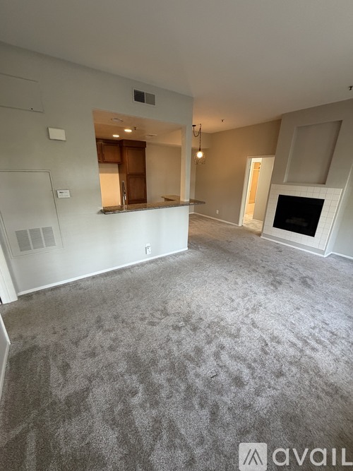 A spacious living room with a fireplace and a kitchen area in the background.