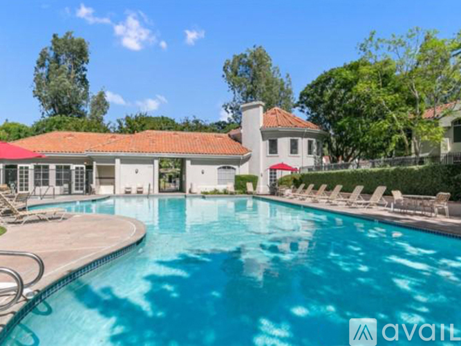 A large swimming pool in front of a house with a red roof.