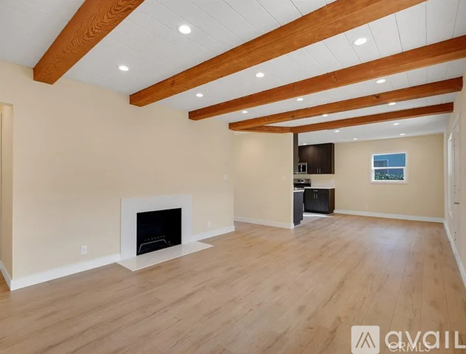 A spacious living room with a fireplace and wooden beams on the ceiling.