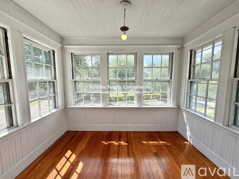 A room with wooden floors and white walls, with windows on three sides.
