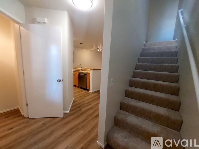 A staircase with a carpeted runner leads up to a landing with a white door and a small kitchenette.
