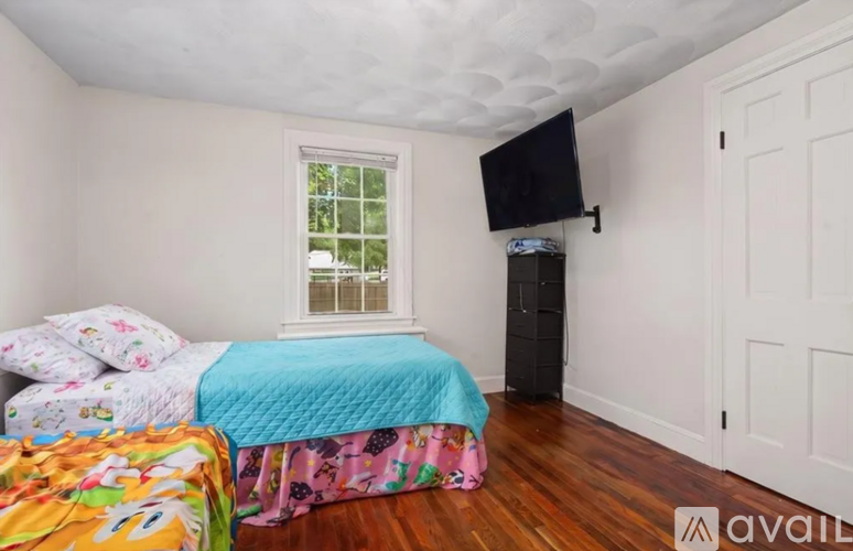 A bedroom with a bed, a window, and a TV mounted on the wall.
