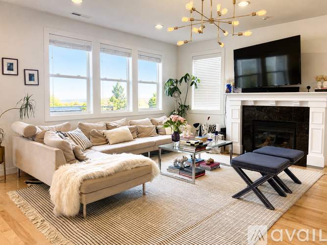 A living room with a white couch, a grey ottoman, a fireplace, and a TV mounted above it.