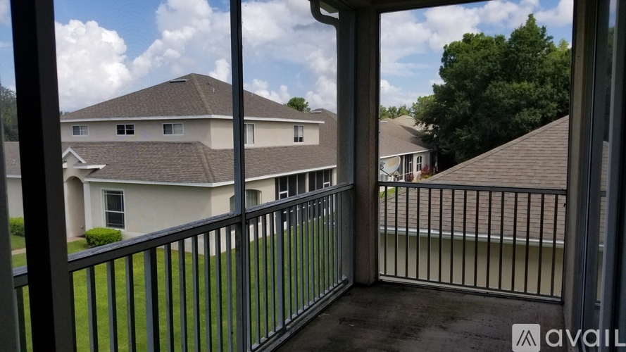 A balcony with a metal railing overlooks a grassy area and houses.