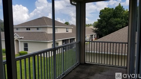 A balcony with a metal railing overlooks a grassy area and houses.