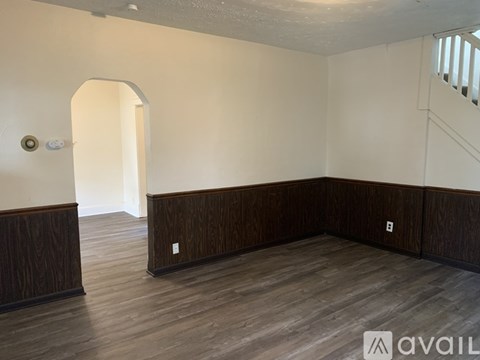 A room with wooden floors and a white wall with a doorway.