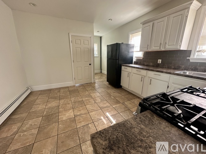 A kitchen with a black refrigerator and brown tiled flooring.
