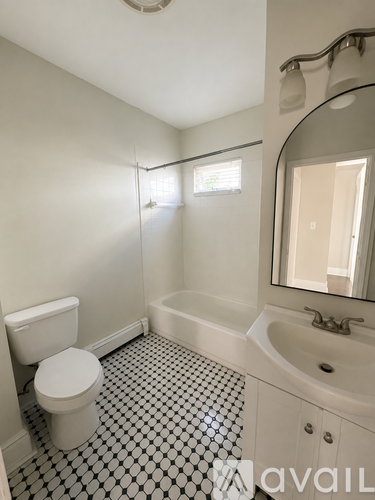 A white toilet sits next to a bathtub in a bathroom with a black and white tiled floor.
