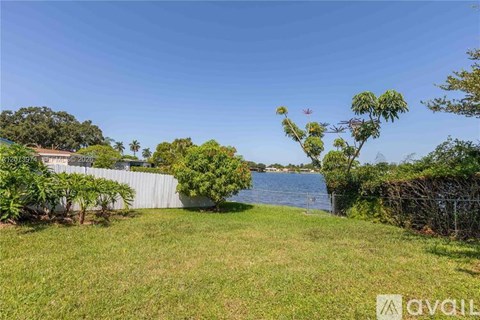 A grassy area with a body of water in the distance and a house on the left.