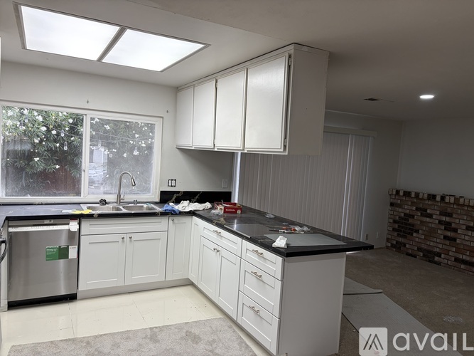 A kitchen with white cabinets and a black countertop is available for rent.