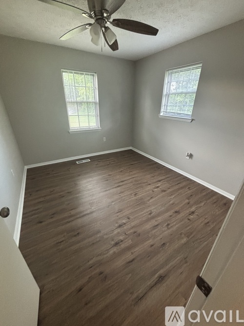 A room with a ceiling fan and two windows.