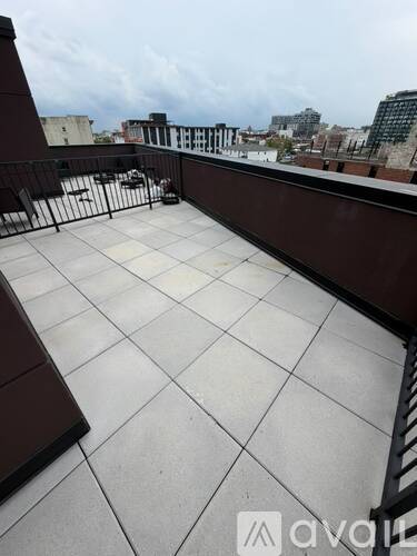 A rooftop patio with a black railing and white tiled floor.