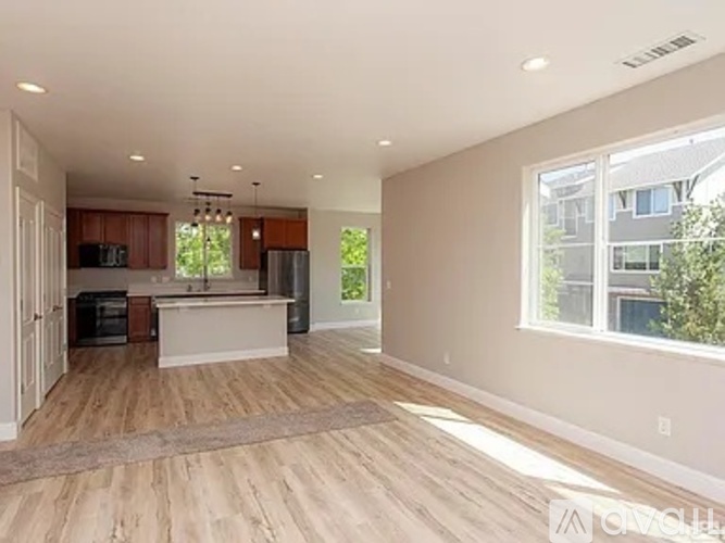 A spacious living room with hardwood floors and a kitchen area in the background.