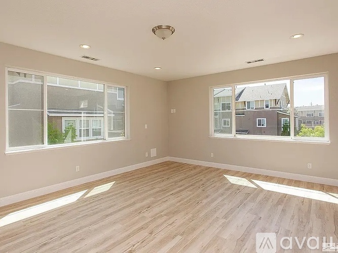 A spacious room with wooden flooring and large windows.