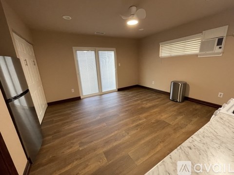 A spacious room with wooden flooring and a refrigerator on the left side.